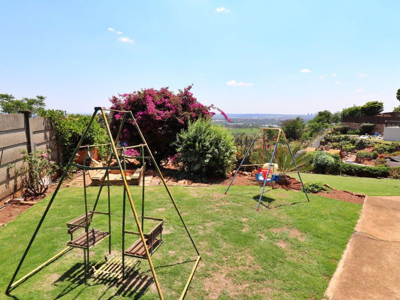 A spacious backyard garden featuring a well-maintained lawn, established landscaping, and a precast concrete boundary wall with scenic distant views.