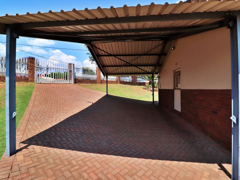 A covered carport area with a paved driveway, brick boundary wall, and secure metal gate access.