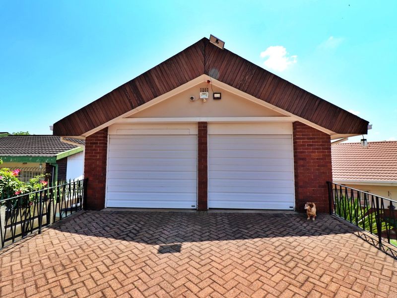 A detached double garage featuring a brick facade, timber gable detailing, and a paved driveway area with metal safety railings.
