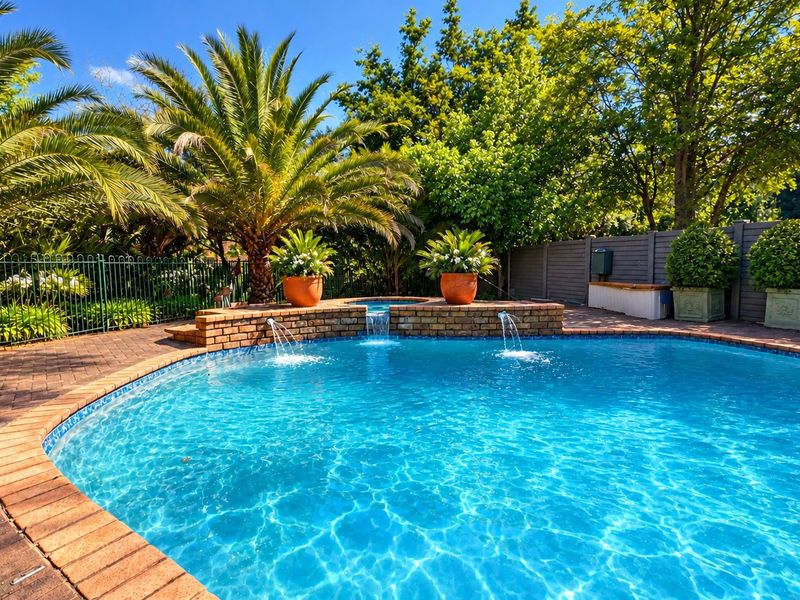 A well-maintained swimming pool area featuring a brick water feature, paved surround, and established garden landscaping, providing a private outdoor retreat.
