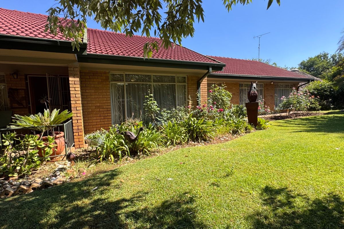 A well-maintained brick house exterior featuring a red tiled roof, a covered patio area, and a lush, established garden.