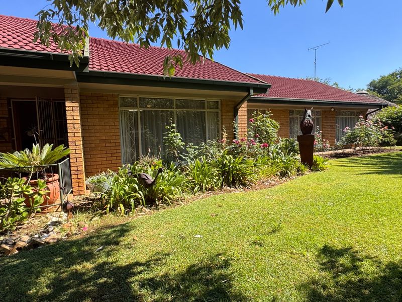 A well-maintained brick house exterior featuring a red tiled roof, a covered patio area, and a lush, established garden.