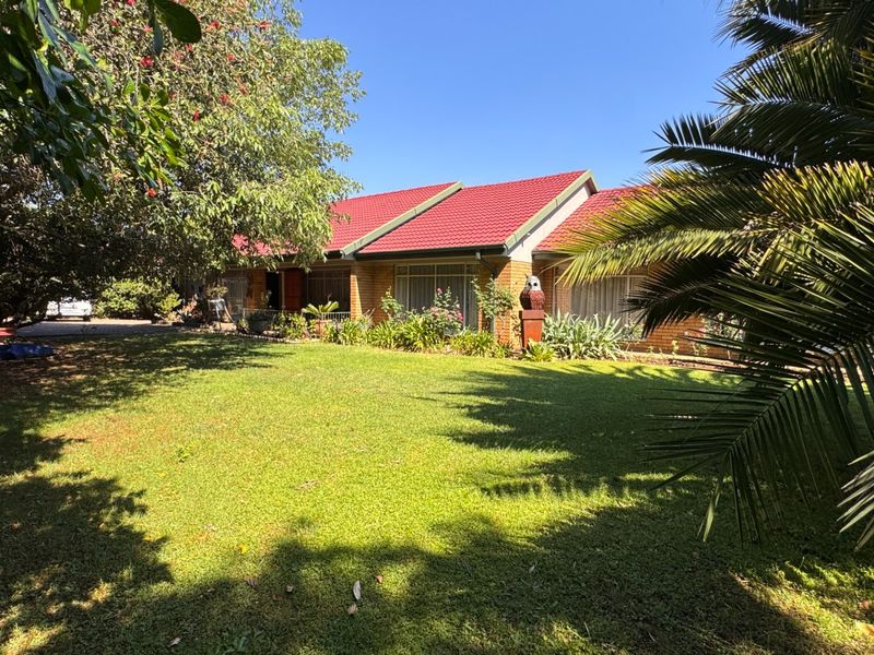A well-maintained single-story brick house featuring a distinctive red tiled roof, set back from the street behind a spacious, lush green front lawn.