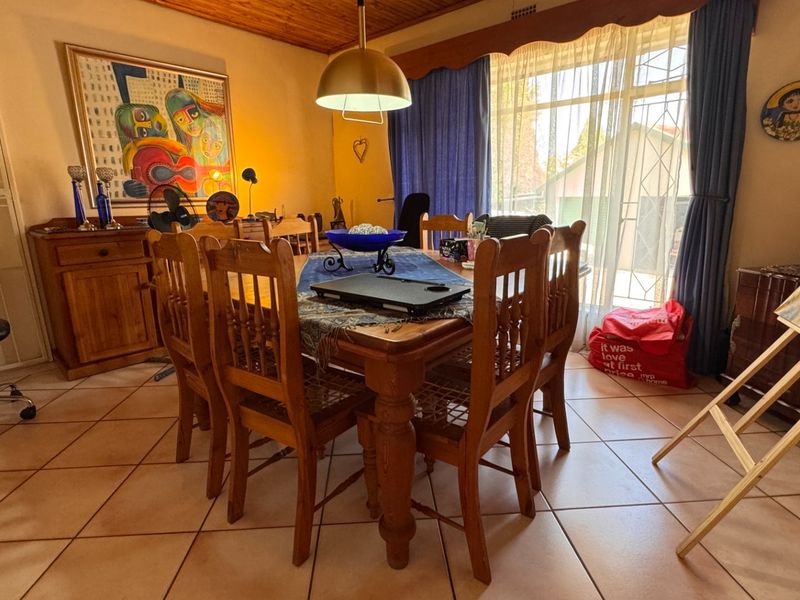 A dining room featuring ceramic floor tiles, a timber ceiling, and a pendant light fixture, with large windows providing natural light.