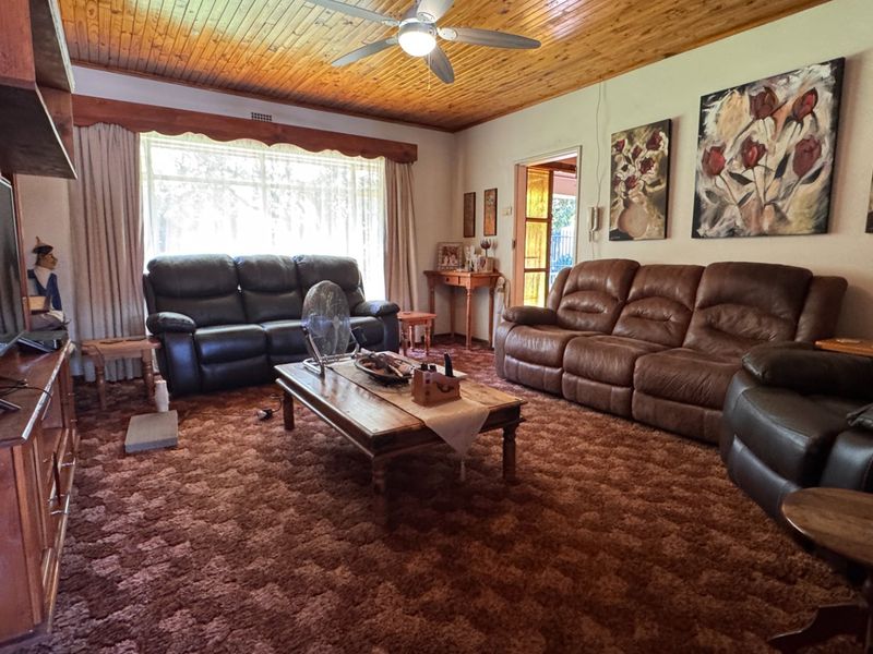 Spacious living room featuring a warm timber tongue and groove ceiling, ceiling fan, and large window allowing for natural light.