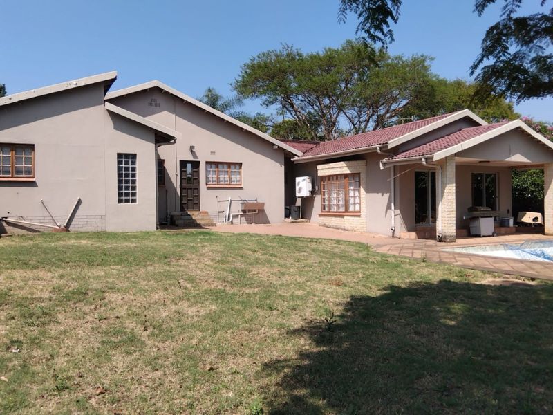 Rear view of the house featuring a paved patio area, swimming pool, and established garden with a tiled roof and exterior wall finishes.