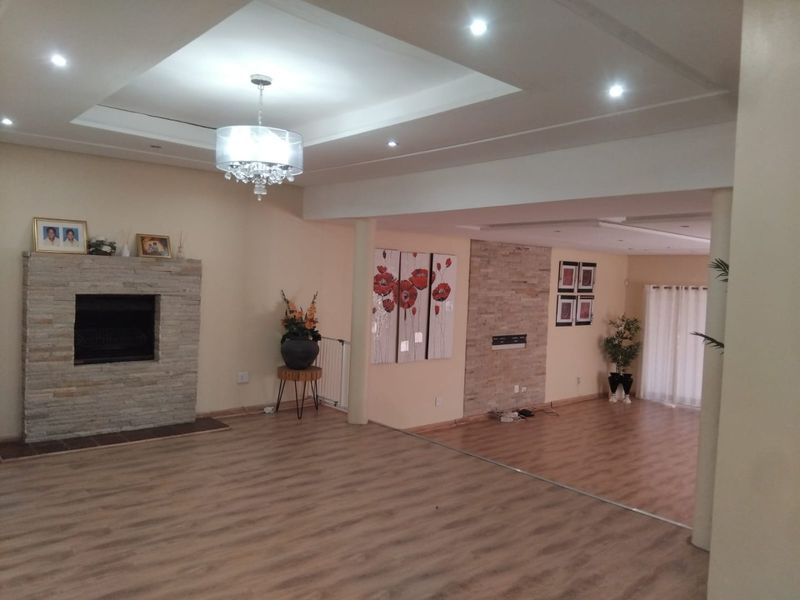 Spacious open-plan living area featuring laminate flooring, a stone-clad fireplace, recessed ceiling details with downlights, and a neutral color palette.