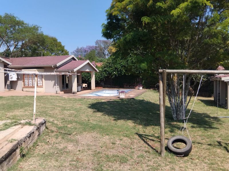 Rear view of the property featuring a swimming pool, covered patio area, and a spacious garden with mature trees.