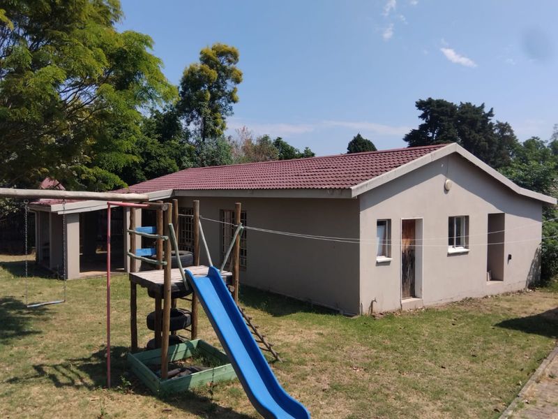 Rear view of the property featuring a tiled roof, plastered exterior walls, and a covered patio area overlooking the garden.