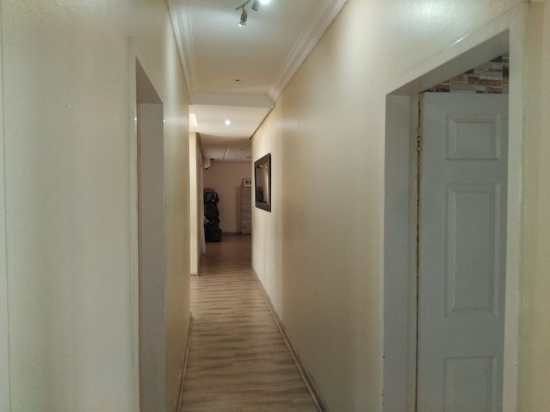 A clean, neutral hallway featuring laminate flooring, coving, and recessed lighting, providing access to multiple rooms within the home.