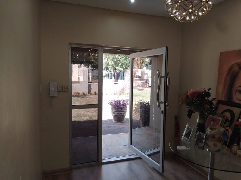 A bright entrance area featuring a modern aluminium glass door, laminate flooring, and an integrated intercom system, providing direct access to the front garden.
