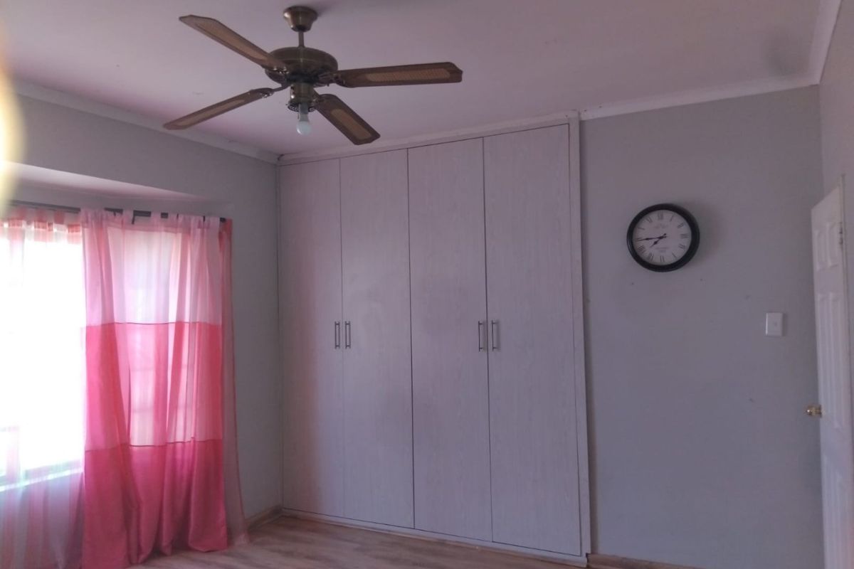 A bedroom featuring built-in cupboards, a ceiling fan, and laminate flooring, offering a clean and functional space.