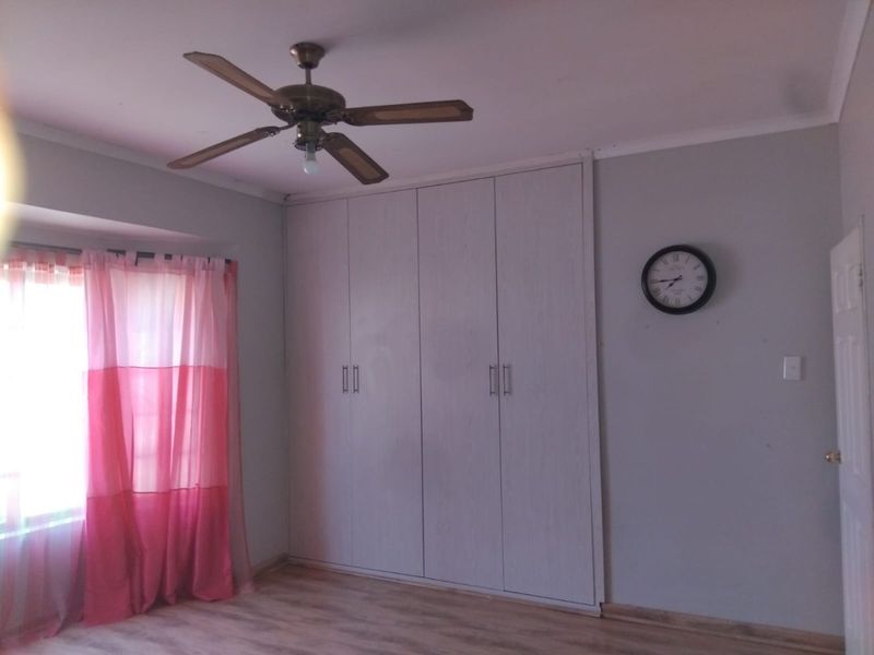 A bedroom featuring built-in cupboards, a ceiling fan, and laminate flooring, offering a clean and functional space.