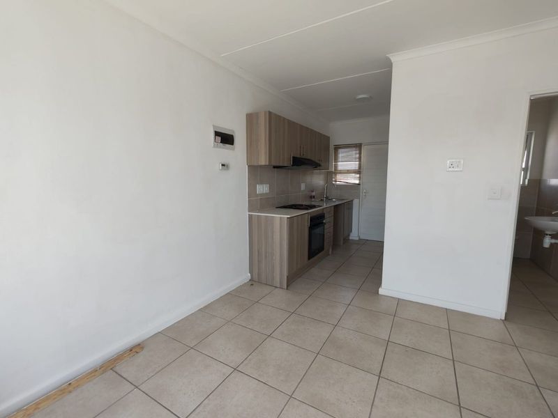 An open-plan living and kitchen area featuring tiled flooring, modern wood-finish cabinetry, and integrated kitchen appliances, presenting a clean and functional space.