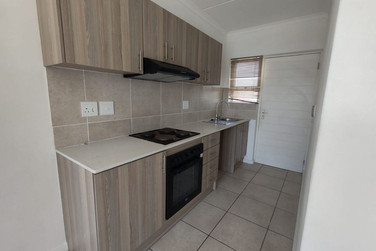 A clean and functional kitchen featuring wood-look cabinetry, built-in oven and hob, extractor fan, and neutral tiled flooring with a convenient rear door access.