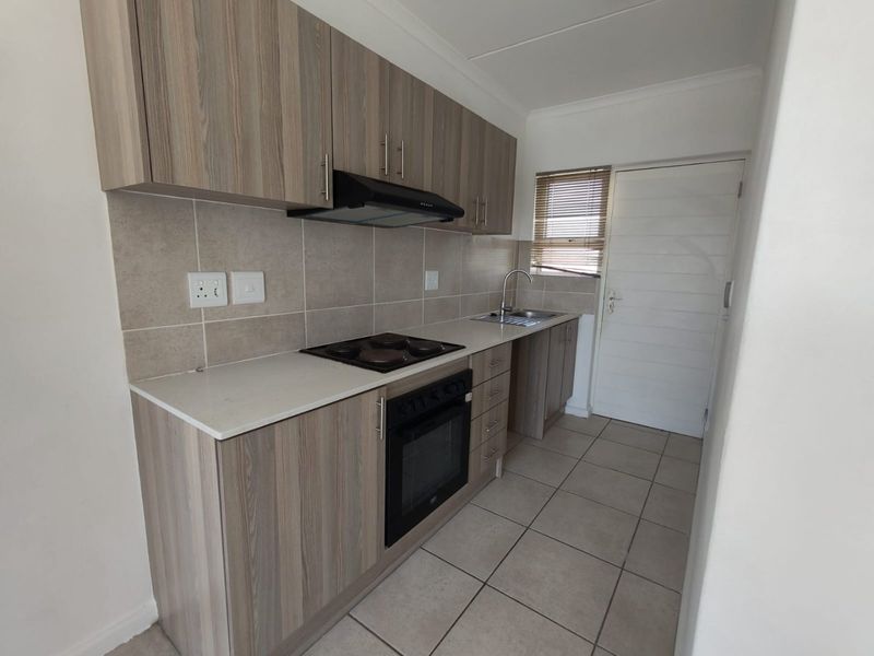 A clean and functional kitchen featuring wood-look cabinetry, built-in oven and hob, extractor fan, and neutral tiled flooring with a convenient rear door access.