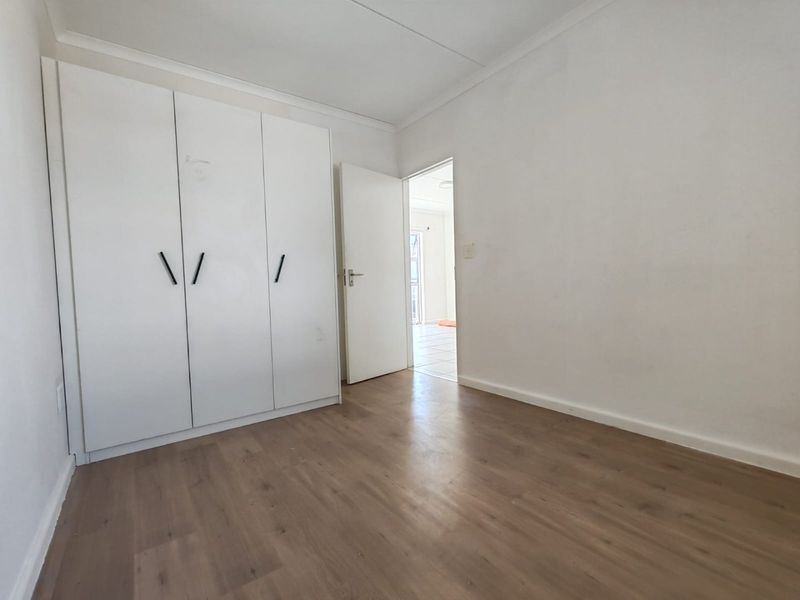 A bright, empty bedroom featuring laminate flooring and a built-in wardrobe, offering a clean and neutral space ready for personalization.