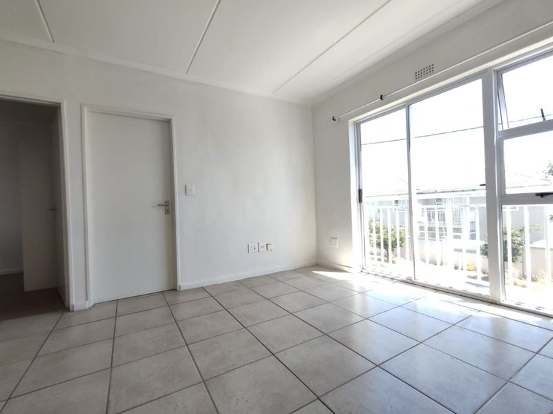 A bright, empty living area featuring neutral tiled flooring and a large sliding glass door providing natural light and access to a balcony.
