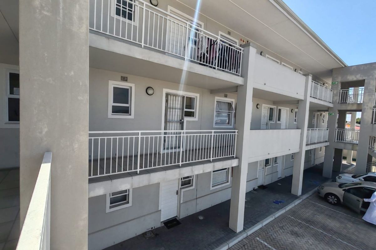 Exterior view of a multi-story apartment complex featuring private balconies with security railings and ground-level paved parking bays.
