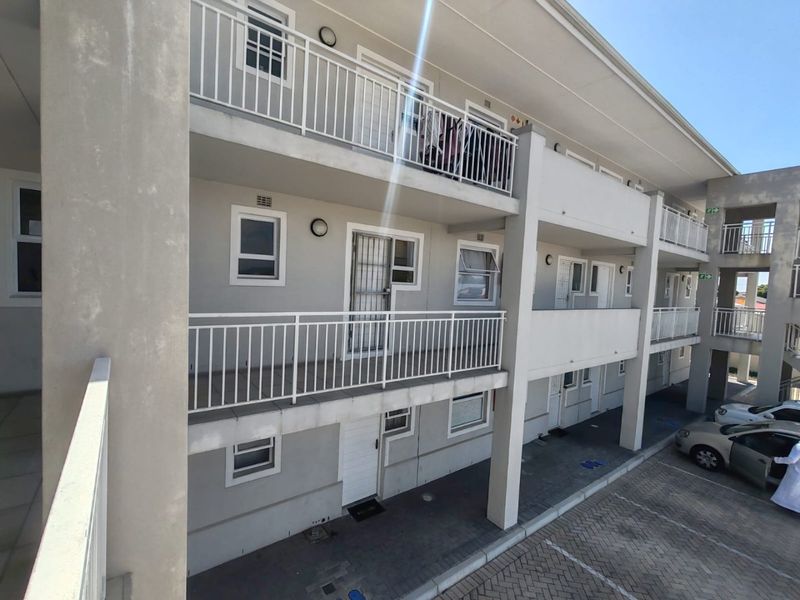 Exterior view of a multi-story apartment complex featuring private balconies with security railings and ground-level paved parking bays.