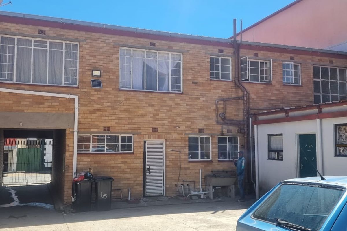 Rear view of a multi-story commercial face brick building featuring steel-framed windows, a concrete driveway, and an integrated covered passage.