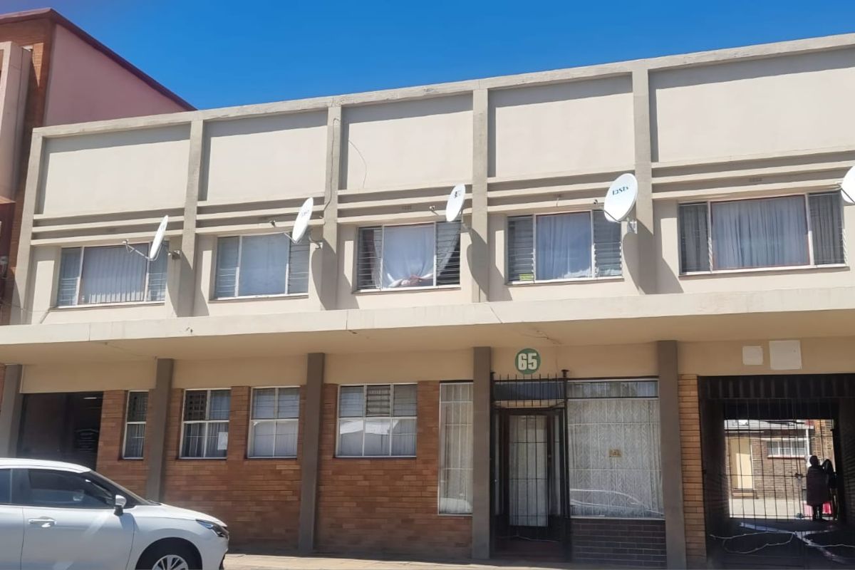 Front elevation of a commercial building featuring a concrete and brick facade with multiple window units and security access.