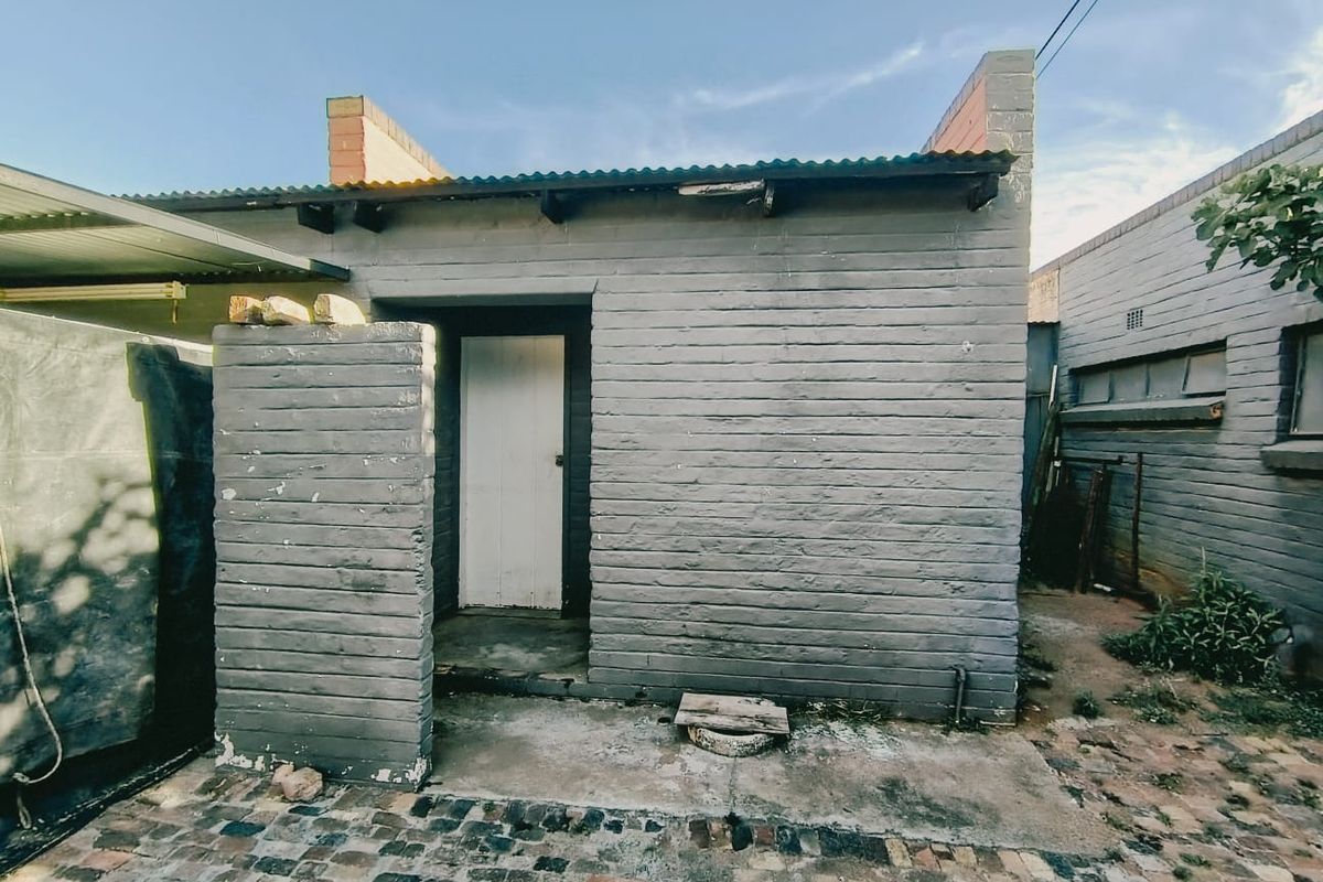 Rear exterior view of a small brick outbuilding featuring a corrugated metal roof and paved courtyard area.