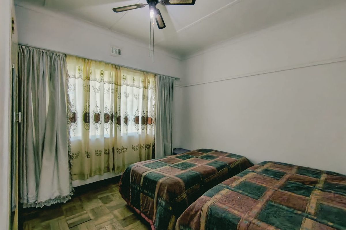 A bedroom featuring classic parquet flooring, a ceiling fan, and large windows with curtain rails, offering a neutral canvas for updates.