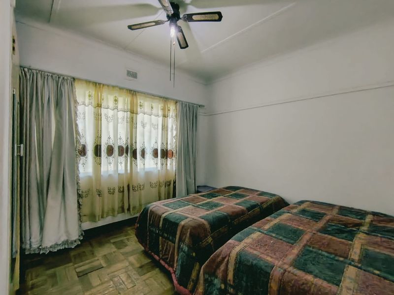 A bedroom featuring classic parquet flooring, a ceiling fan, and large windows with curtain rails, offering a neutral canvas for updates.