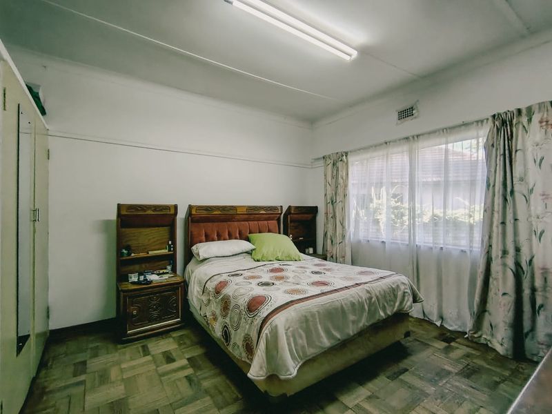 A bedroom featuring parquet flooring, a built-in wardrobe, and a large window with natural light.