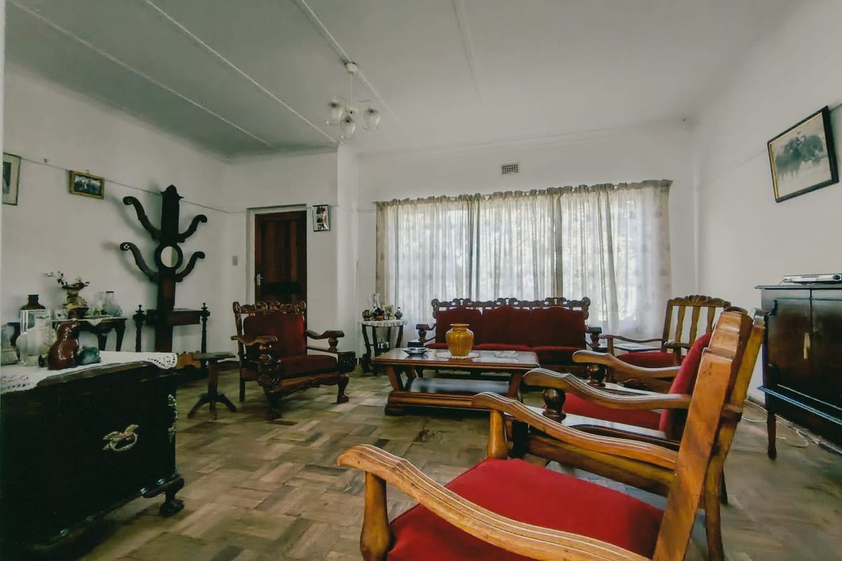 A spacious living room featuring classic parquet flooring, traditional cornicing, and a central ceiling light fixture, offering a warm and character-filled living space.