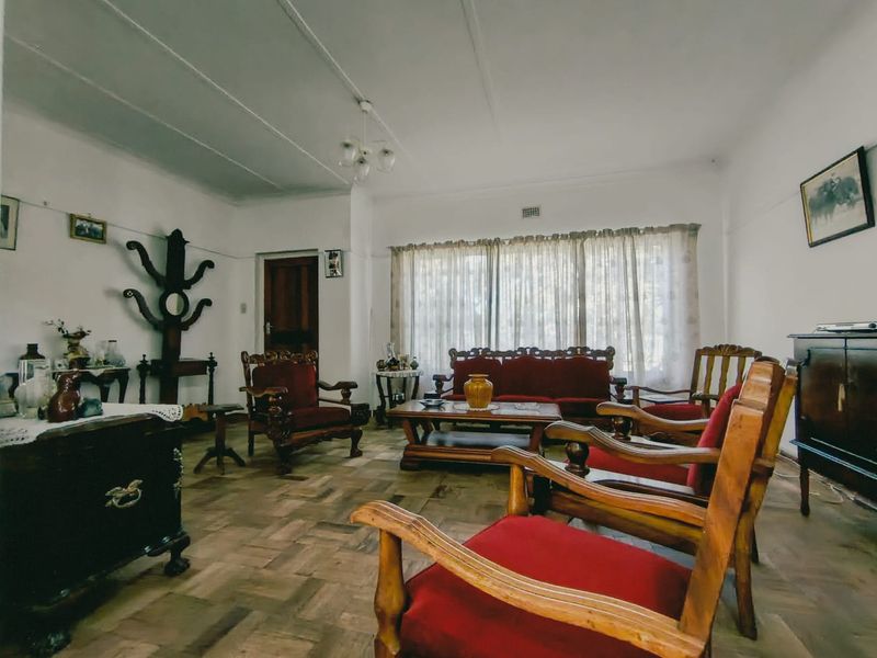 A spacious living room featuring classic parquet flooring, traditional cornicing, and a central ceiling light fixture, offering a warm and character-filled living space.