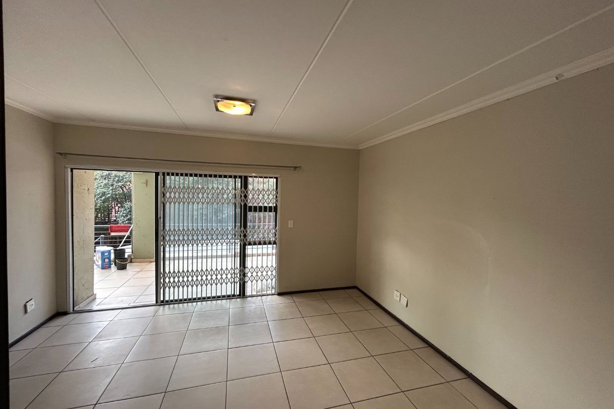 An empty, neutrally painted living room featuring tiled flooring, a ceiling light, and a sliding glass door with a security gate leading to a patio.