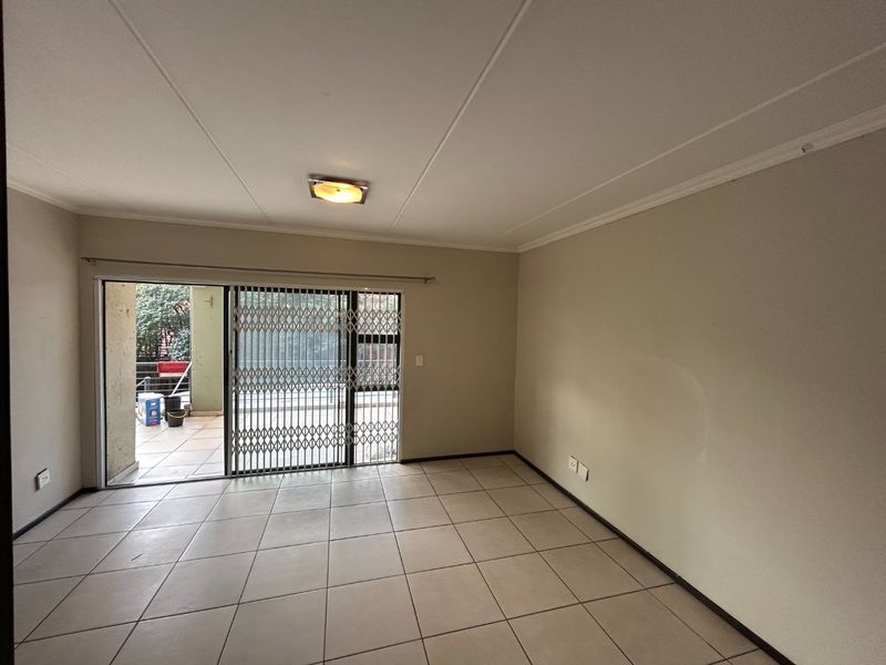 An empty, neutrally painted living room featuring tiled flooring, a ceiling light, and a sliding glass door with a security gate leading to a patio.