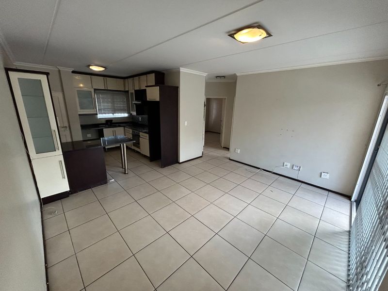 An open-plan living and kitchen area featuring tiled flooring, built-in cabinetry, a breakfast counter, and direct access to an outdoor space via sliding doors.