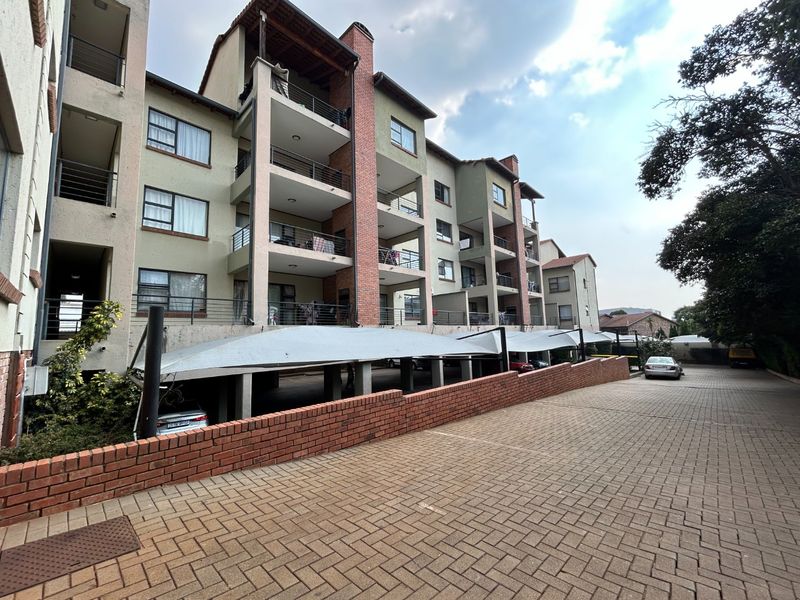 Exterior view of a multi-story apartment complex featuring brick paving, covered parking bays, and private balconies with metal railings.