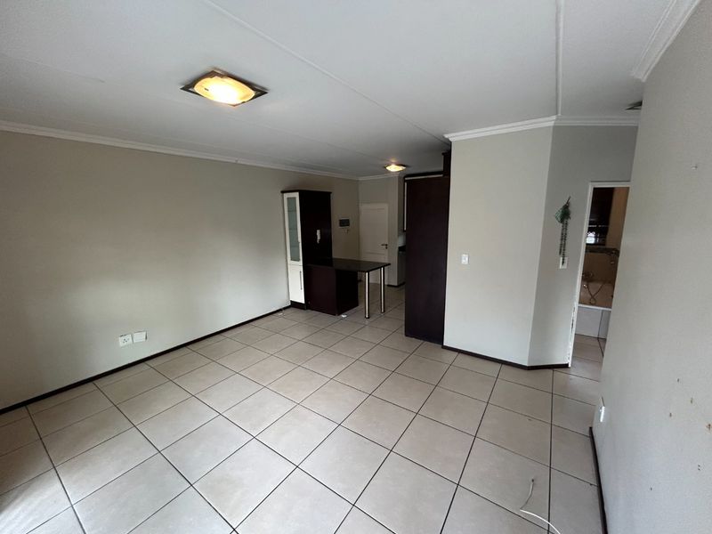 An open-plan living area featuring neutral tiled flooring, built-in cabinetry with a breakfast counter, and access to an adjacent bathroom.