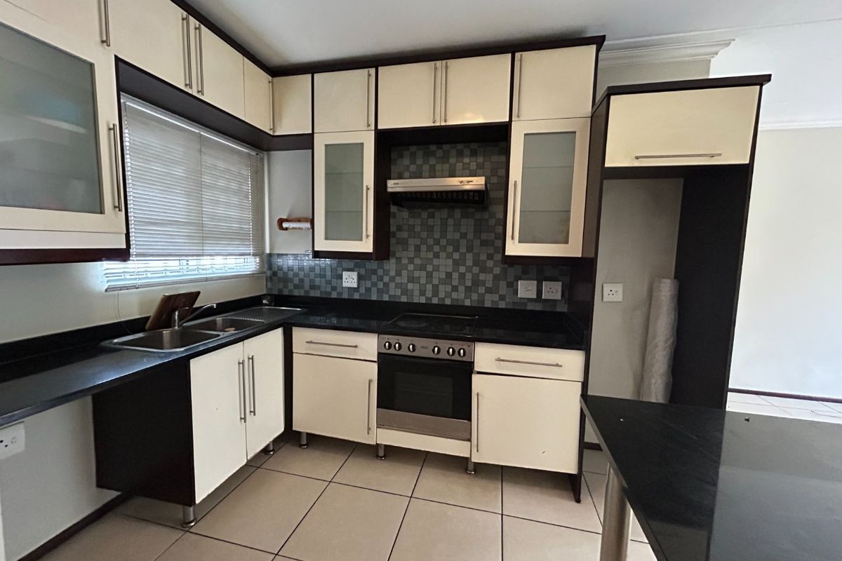 A functional kitchen featuring two-tone cabinetry, granite countertops, a built-in oven with extractor fan, and tiled flooring.