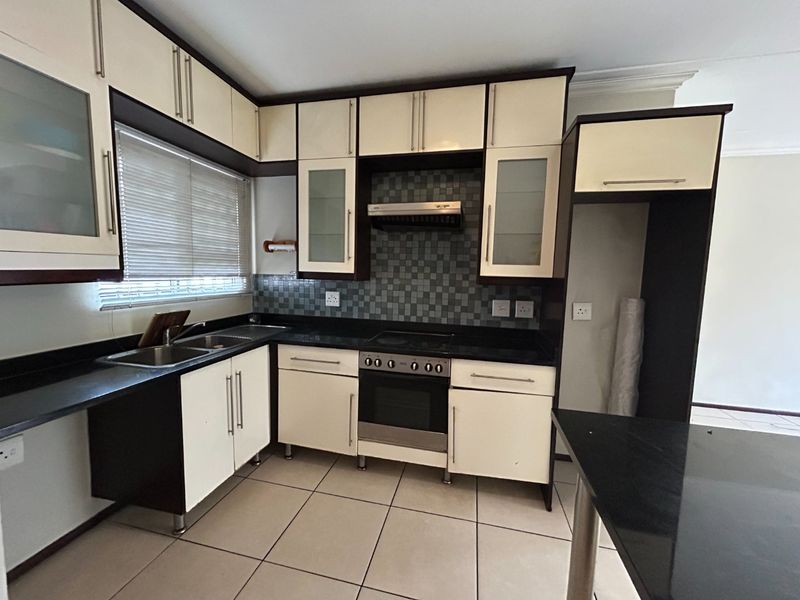 A functional kitchen featuring two-tone cabinetry, granite countertops, a built-in oven with extractor fan, and tiled flooring.