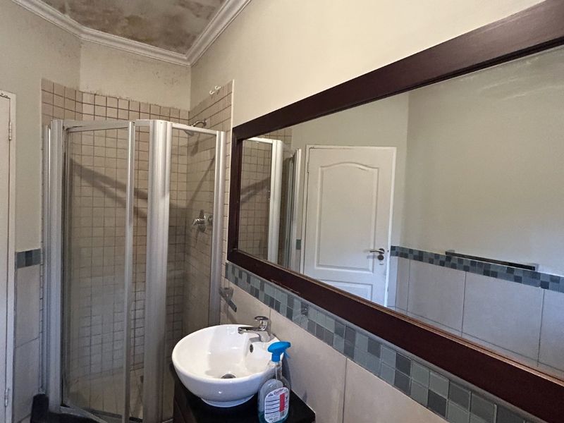 Bathroom featuring a corner shower enclosure, vessel sink with vanity cabinet, and large wall mirror, requiring ceiling repairs due to visible water damage.