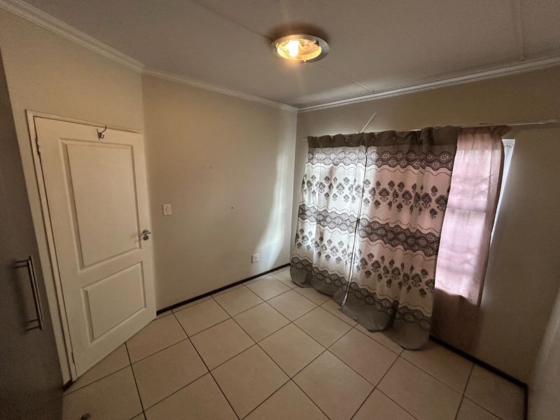 A vacant bedroom featuring neutral tiled flooring, a ceiling light fixture, and a panel door, offering a blank canvas for personalization.