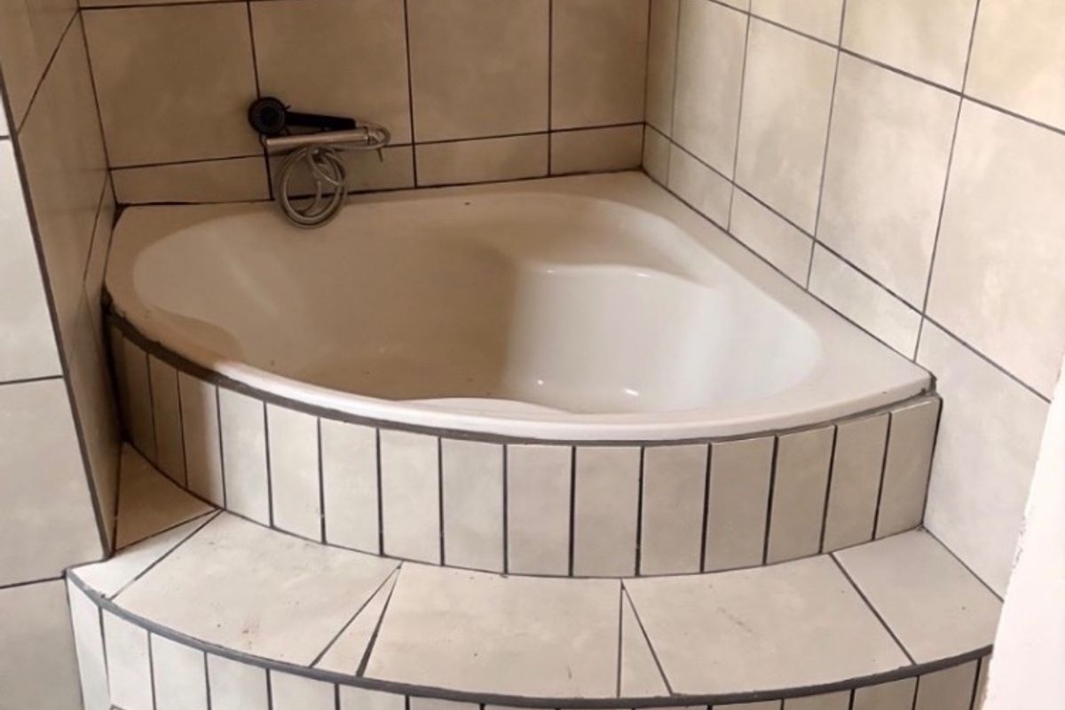 A dated corner bathtub featuring tiled steps and wall-mounted fixtures, requiring cosmetic updates to modernize the bathroom space.