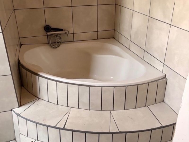 A dated corner bathtub featuring tiled steps and wall-mounted fixtures, requiring cosmetic updates to modernize the bathroom space.