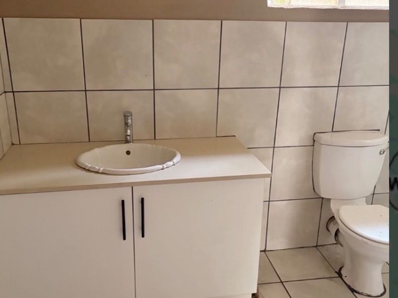 A functional bathroom featuring a vanity cabinet with a drop-in basin, a standard toilet, and tiled finishes throughout.