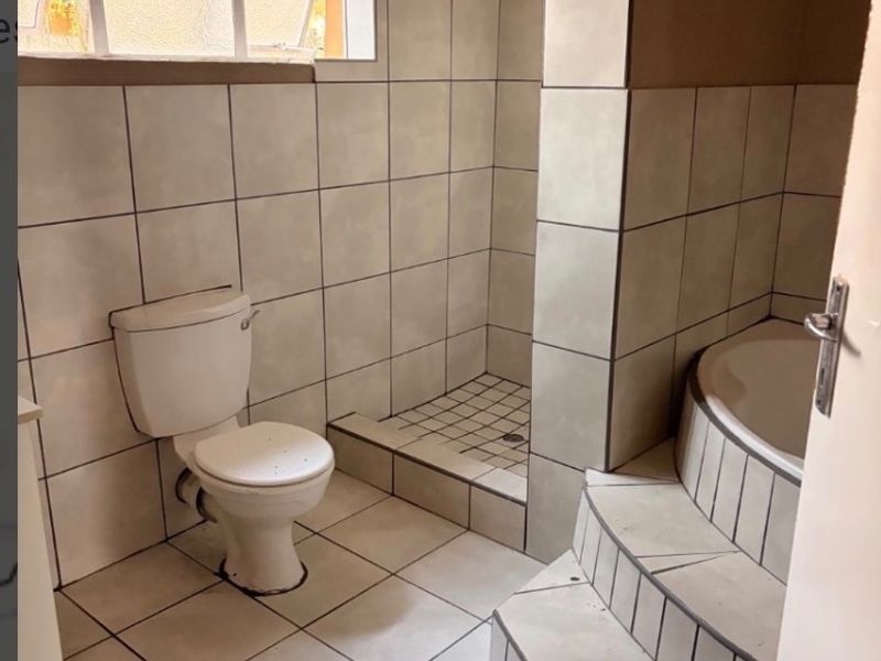 A dated bathroom featuring a built-in bathtub with tiled steps, a separate shower enclosure, and a toilet, requiring cosmetic updates to finishes.