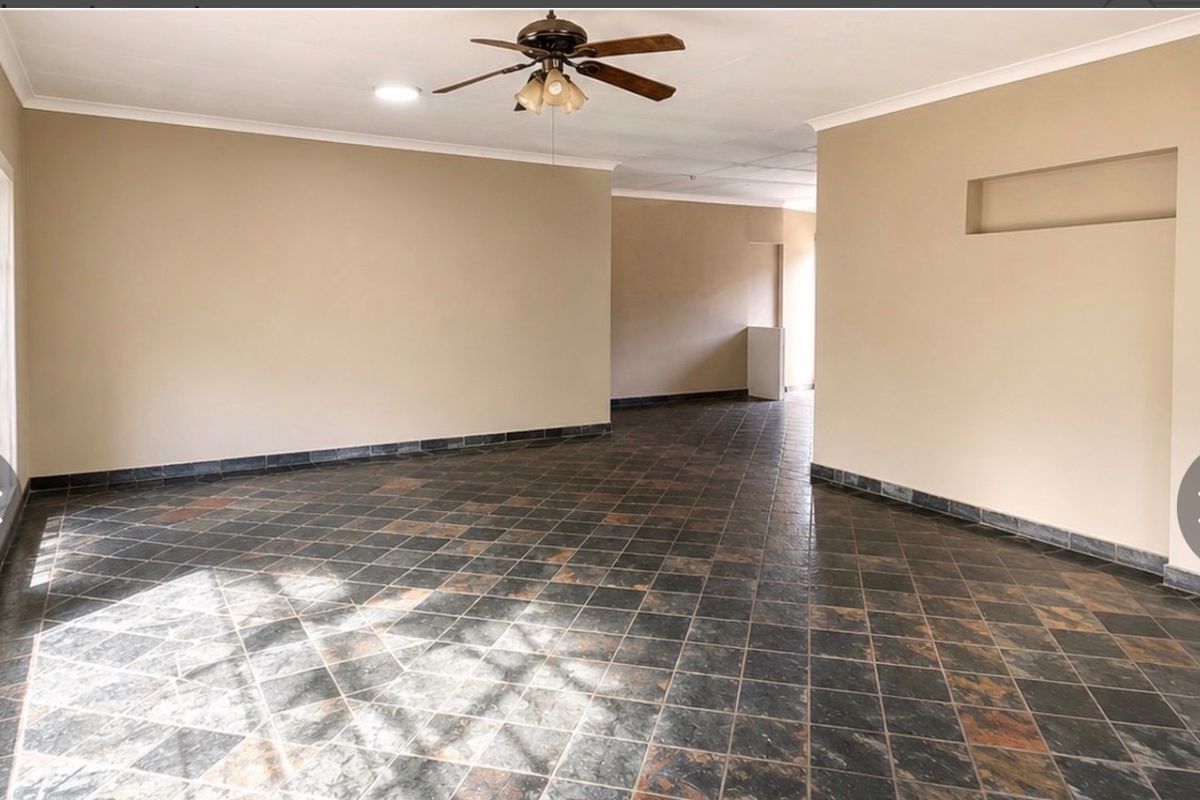 A spacious, empty living area featuring dark tiled flooring, a ceiling fan, and a built-in wall niche, offering a neutral canvas for interior design.