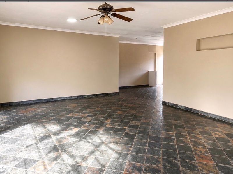 A spacious, empty living area featuring dark tiled flooring, a ceiling fan, and a built-in wall niche, offering a neutral canvas for interior design.
