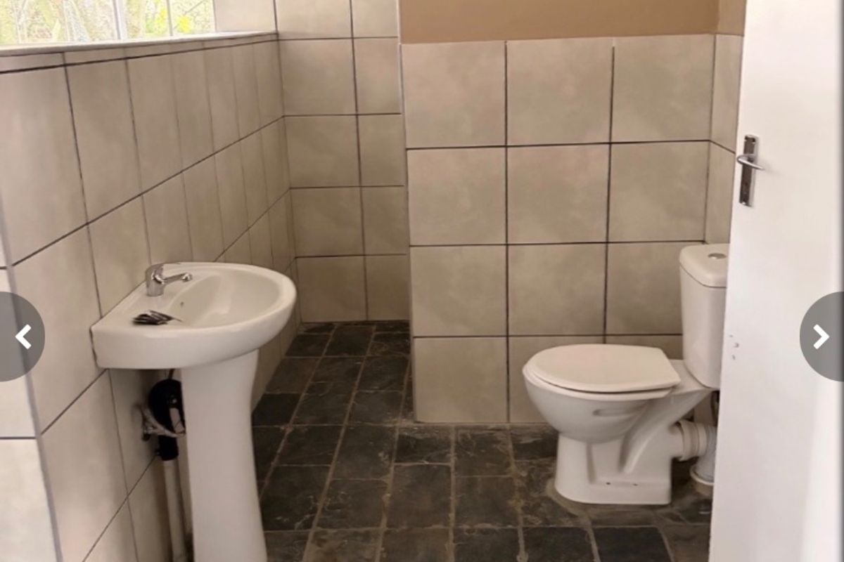 A functional bathroom featuring a pedestal basin, ceramic toilet, and tiled finishes. The space is currently vacant and requires cosmetic updates.