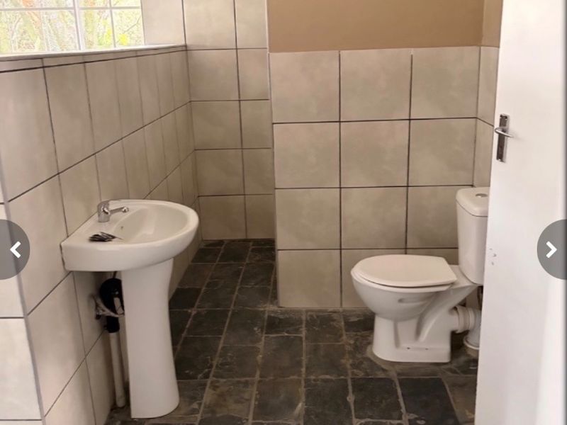A functional bathroom featuring a pedestal basin, ceramic toilet, and tiled finishes. The space is currently vacant and requires cosmetic updates.