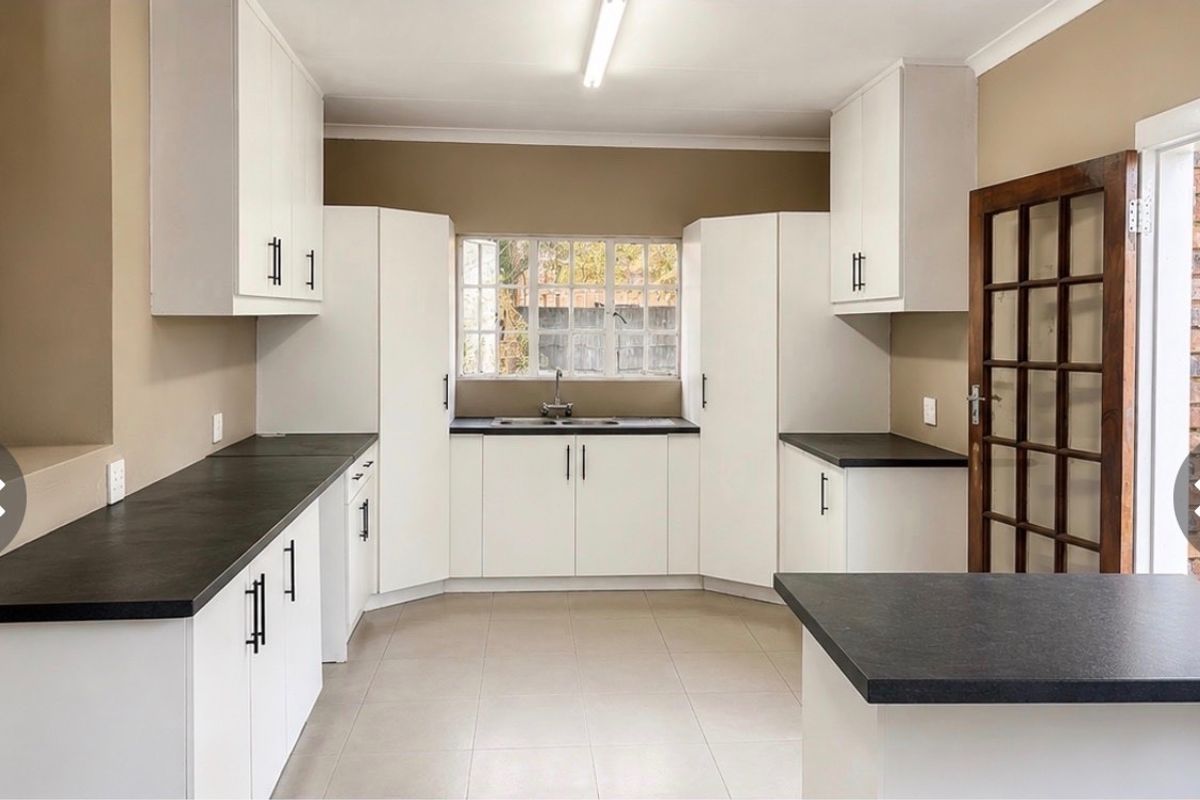 A clean and functional kitchen featuring white cabinetry, dark countertops, tiled flooring, and direct access to the exterior through a timber framed glass door.